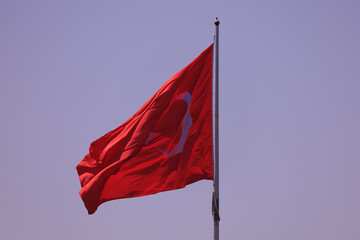 Turkish flag, on a red background white star and moon. Flag flies in the wind, public place.