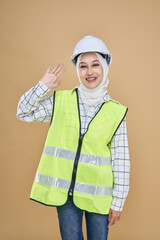 Asian hijab girl engineer in yellow  vest and wearing a safety helmet, give a  hand gesture isolated on background in studio.