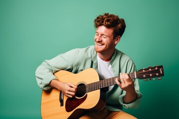 Portrait of a glad man in his 20s playing the guitar over pastel green background