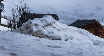 Tas de neige entassé devant des chalets en hiver dans les Alpes à la Toussuire par une journée avec du brouillard