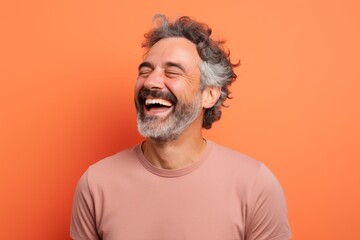Obraz premium Portrait of a satisfied man in his 40s laughing in front of pastel orange background