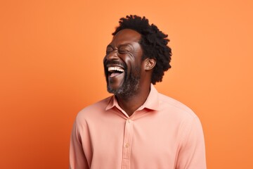 Obraz premium Portrait of a jovial afro-american man in his 40s laughing isolated on pastel orange background