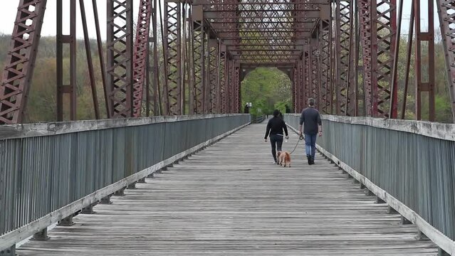 couple walking on the north county trail across the putnam railroad bridge over the croton reservoir in the hudson valley (man woman dog) steel bridge with wooden path trail