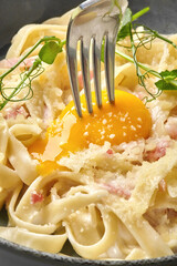 Fork breaking golden egg yolk on carbonara pasta