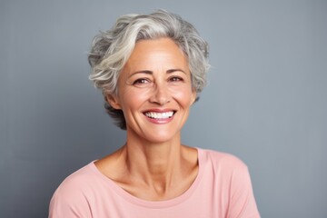 Fototapeta premium Portrait of a glad woman in her 50s smiling at the camera isolated in pastel gray background