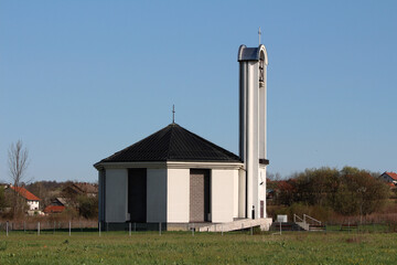 Newly built modern white and grey catholic church tall bell tower with iron cross on top and large...