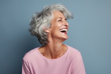 Portrait of a content woman in her 50s laughing on pastel gray background