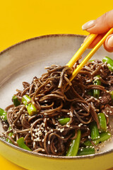 Female hand picking up beef soba noodles using chopsticks