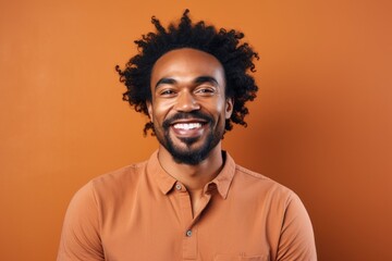 Portrait of a merry afro-american man in his 30s smiling at the camera isolated in pastel brown background