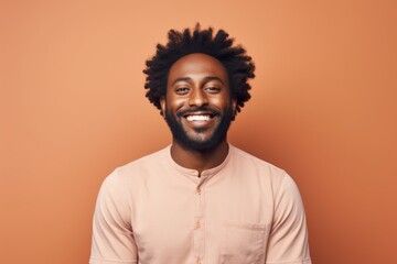 Fototapeta premium Portrait of a merry afro-american man in his 30s smiling at the camera isolated on pastel brown background