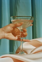 Female hand holding a martini glass on a background of a curtain.