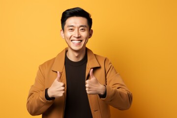 Portrait of a content asian man in his 30s showing a thumb up in front of pastel brown background
