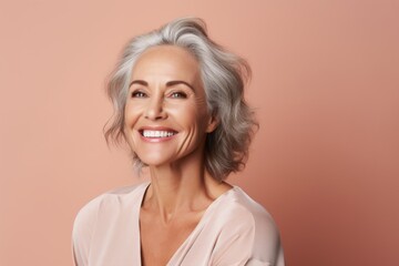 Fototapeta premium Portrait of a blissful woman in her 50s smiling at the camera in front of pastel brown background