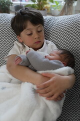 A young boy lovingly holds his newborn sibling, creating a serene and affectionate moment that...