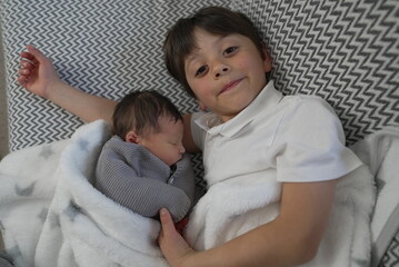 A young boy and his newborn sibling snuggle together, radiating warmth and love, showcasing the...