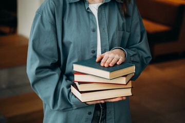 Young woman with a pile of books on a blurred library background.