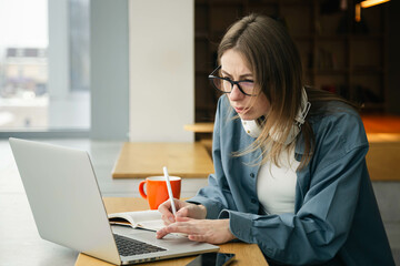 A young woman with glasses sits in front of a laptop and studies, copy space.