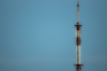 Obraz premium A tall communication tower painted red and white stands against a clear blue sky, emphasizing its towering presence.