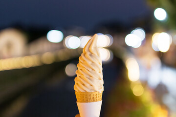 Close-up of a hand holding an ice cream cone with a blurred background of lights.