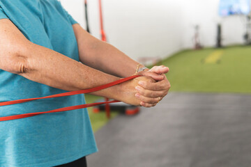 An adult woman stretches holding a red elastic band in the gym.