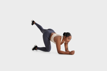 African American woman is seen exercising on a plain white background. She is engaged in physical...