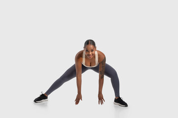 African American woman is seen performing a squat exercise on a white background. She is bending...