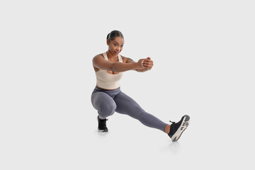 African American woman is shown doing a squat exercise on a plain white background. She is bending...