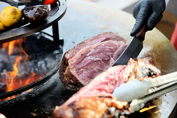 A large pieces of raw fresh steak are grilling on flaming grill.