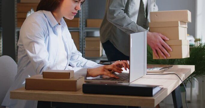 Young business woman laptop working online, individual seller starting small family business. Warehouse man, woman at storing area, marketplace manager checking box item title, description and price