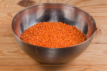 Raw red lentil in stainless steel bowl on rustic table