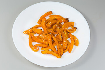 Baked slices of butternut squash on dish on gray background