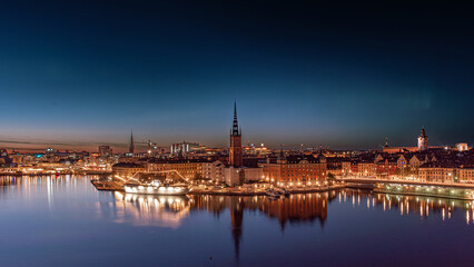 Stockholm, Riddarholmen, the old town, at night in summer, green aurora borealis, nothern lights partly visible in the sky. Orange and yellow city lights, medieval buildings, churches and city skyline