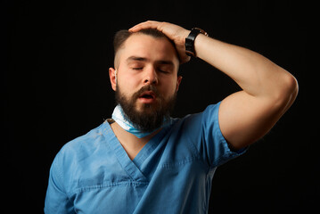 A doctor in a blue coat has taken off his mask and is running his hand over his head from fatigue after his shift. Grain effect used