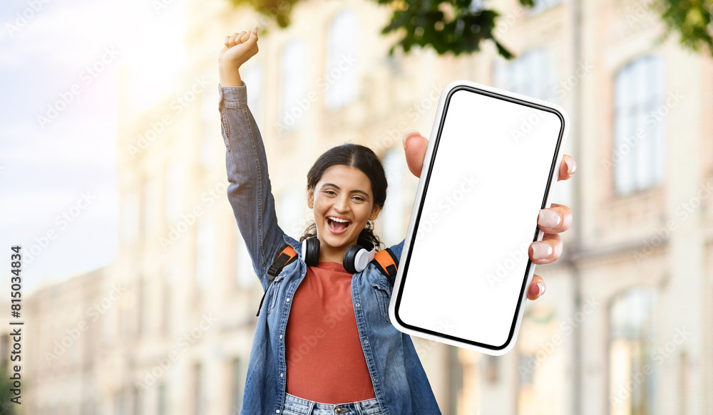 Poster hindu woman is standing and holding up a smartphone with a blank screen. she is looking at the phone