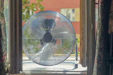 Close up of a big metal fan on the windowsill.