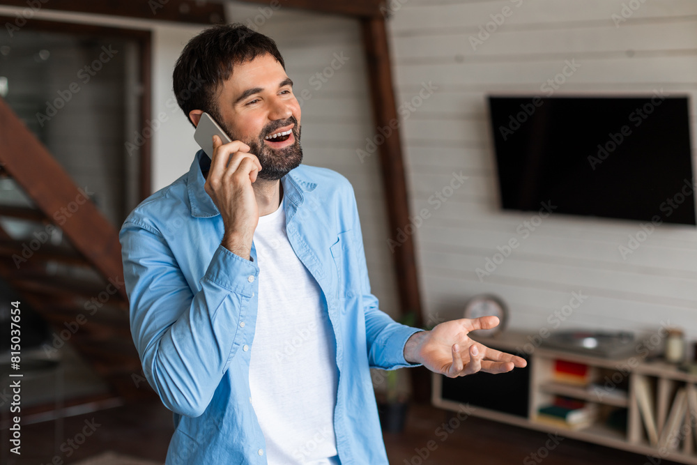 Poster a man is having a conversation on a cell phone while standing in a living room. there is a couch and