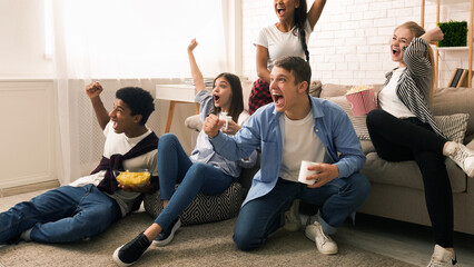A group of friends is gathered in a cozy living room, expressing joy and excitement. Some are...
