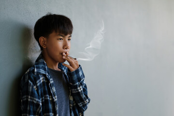 Teenager underage smoking a cigarette causes bad habits causing addiction. Asian kid smoking behind the school, feeling sad, unhappy, stressed in an old dirty grungy place.