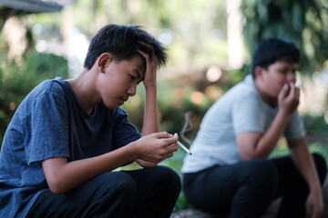 Teenagers underage smoking a cigarette causes bad habits causing addiction. Asian kid smoking behind the school, feeling sad, unhappy, stressed in an old dirty grungy place.