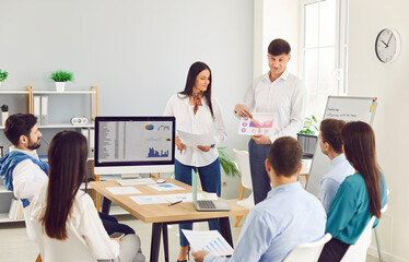 Obraz premium Young business man talking about work project for a group of company employees sitting at the desk in meeting room. Confident business people discussing company growth on a conference in office.