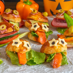 Monster sandwich made with cheese, salmon, lettuce leaves and fresh buns for Halloween on textured paper. Kid's food ideas for Halloween.