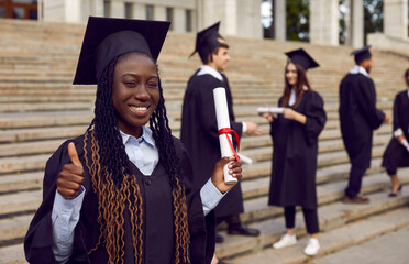 Young happy smiling african american female student in a university graduate gown and diploma in...