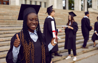 Young happy smiling african american female student in a university graduate gown and diploma in...