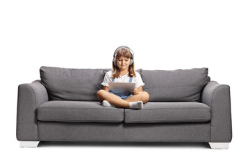 Obraz premium Kid with headphones sitting on a sofa and using a digital tablet