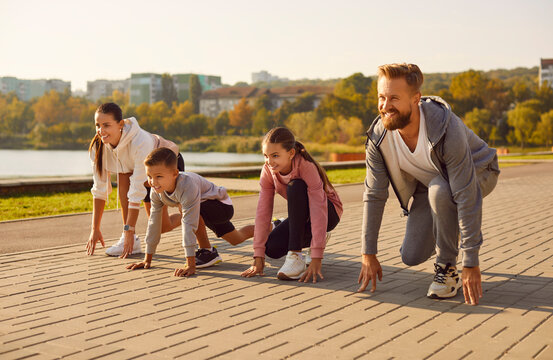 Happy family having outdoor sports workout on city street. Smiling mother, father and children getting ready to start running. Sporty mum, dad and kids all in line ready to compete in sprint distance