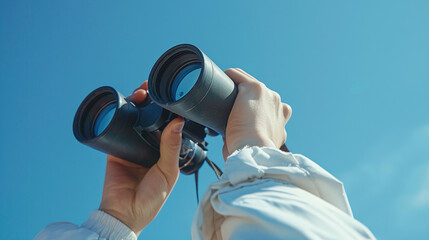 Obraz premium Person Holding Black Binoculars Against Clear Blue Sky Exploring Vast Horizons