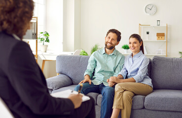 Happy smiling young couple sitting on the couch at counselor's office, listening advices and...