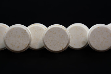 White pills on a black background. Focus on foreground, shallow depth of field.