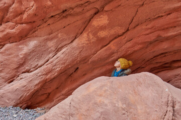 Latino boy's head with woven cap looking up, behind a rock formation hiking in Jujuy, Argentina