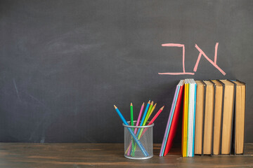 Colorful notebooks and pencils, study books on wooden table in front of blackboard with Hebrew...